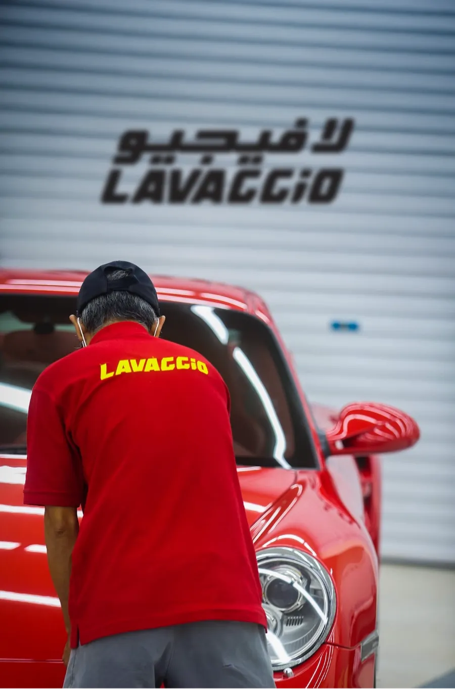 A Lavaggio technician inspecting a red sports car in front of the Lavaggio sign